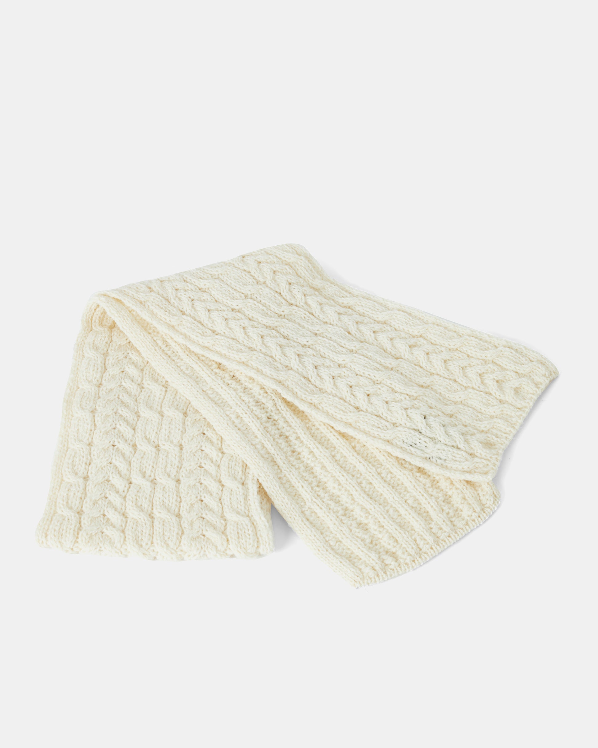 A folded, cream-colored knitted scarf made from Heritage Worsted Wool with a cable knit pattern, displayed on a white background. The unisex-scarf's detailed texture and neat folds are visible, highlighting its cozy and warm appearance. Introducing the Aran Irish Knit Cable Scarf - B386 by Mjölkshop.se.