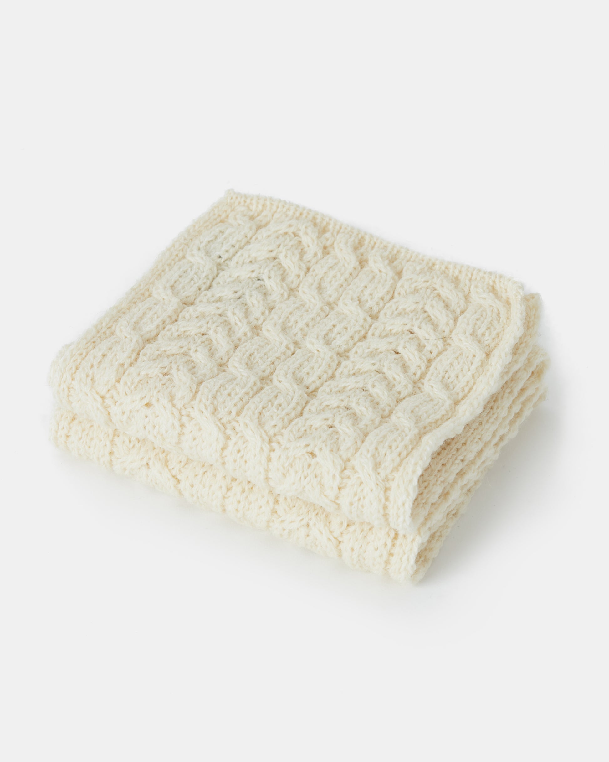 A folded cream-colored, cable-knit blanket made from Heritage Worsted Wool is displayed against a plain white background. The soft texture and intricate patterning of the blanket are clearly visible.

Replaced:
A folded cream-colored, cable-knit Aran Irish Knit Cabel Scarf - B386 from Mjölkshop.se is displayed against a plain white background. The soft texture and intricate patterning of the scarf are clearly visible.