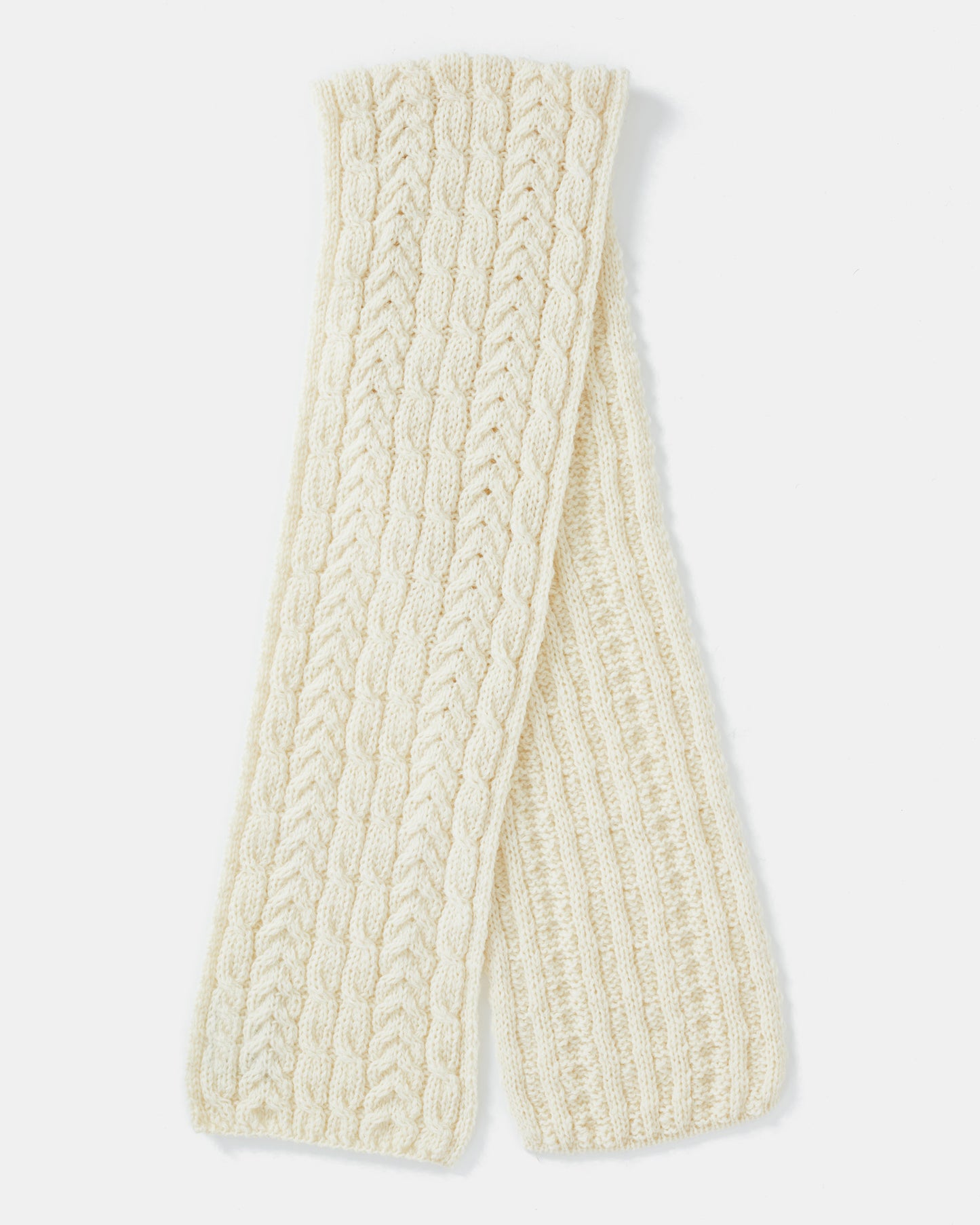 A cream-colored knitted unisex-scarf crafted from Heritage Worsted Wool, featuring a textured pattern with alternating cable and ribbed designs. The scarf is neatly folded, displaying its intricate detailing and soft, cozy material. The plain white background highlights the scarf's craftsmanship. This is the Aran Irish Knit Cable Scarf - B386 from Mjölkshop.se.