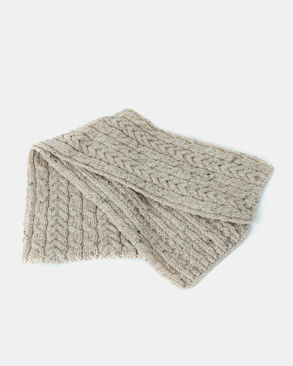 A folded beige knit scarf with a detailed cable pattern is displayed against a white background. The unisex-scarf's texture is clearly visible, showcasing the intricate knitting design made from Heritage Worsted Wool. This beautiful piece is the Aran Irish Knit Cabel Scarf - B386 from Mjölkshop.se.