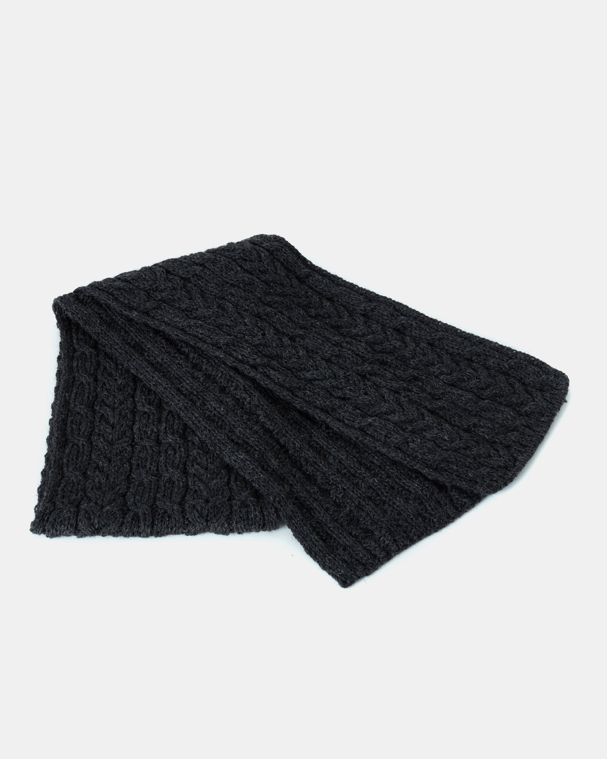 A folded dark gray knitted unisex-scarf with a cable pattern design is displayed against a plain white background. Made from Heritage Worsted Wool, the Aran Irish Knit Cabel Scarf - B386 from Mjölkshop.se's texture appears soft and warm, making it suitable for cold weather.