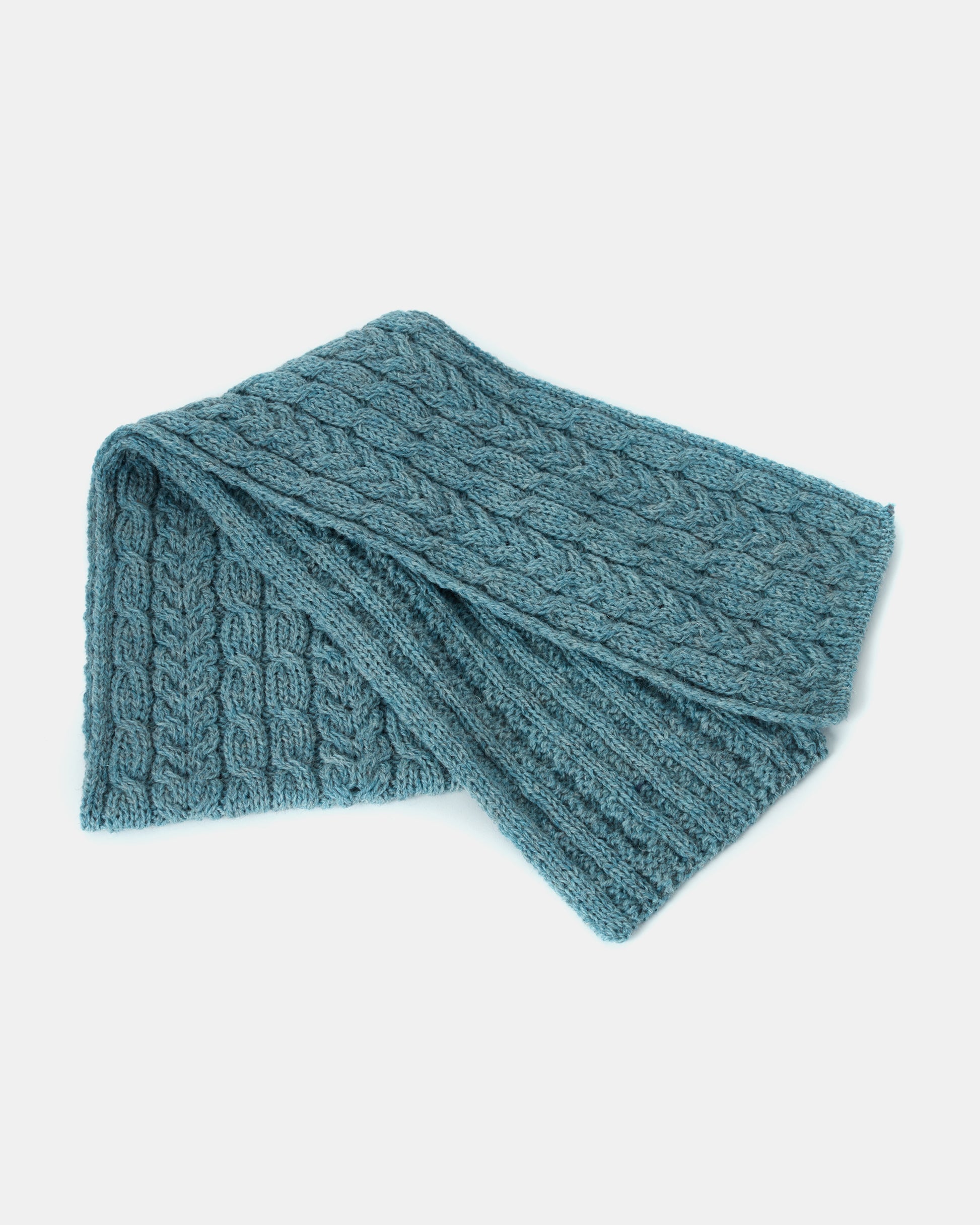 A folded, blue knitted unisex-scarf with a cable pattern design on a white background, crafted from Heritage Worsted Wool, Mjölkshop.se Aran Irish Knit Cable Scarf - B386.