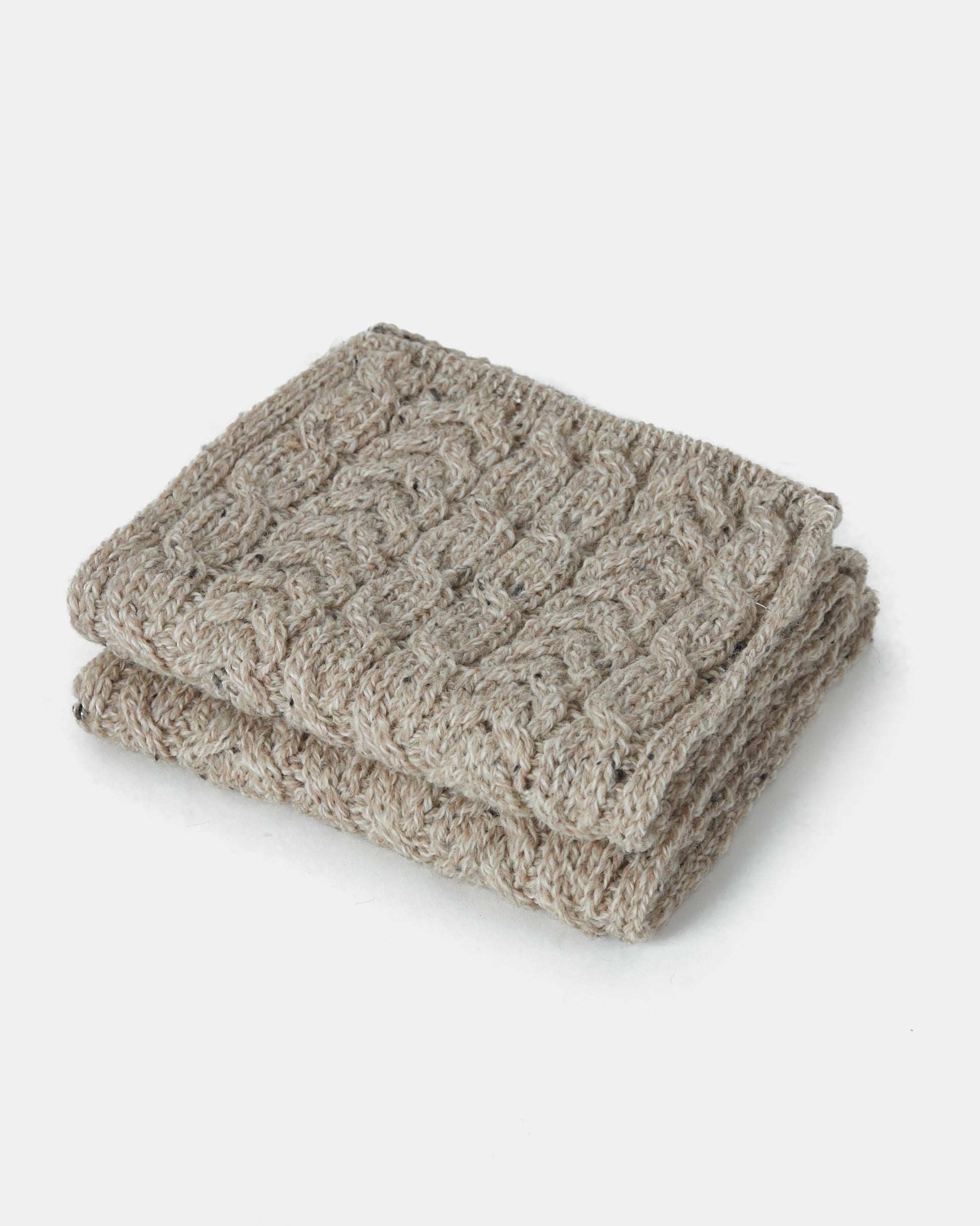 A folded beige Aran Irish Knit Cabel Scarf - B386 from Mjölkshop.se made from Heritage Worsted Wool with a textured pattern of alternating cable and ribbed stitches, placed on a plain white background.