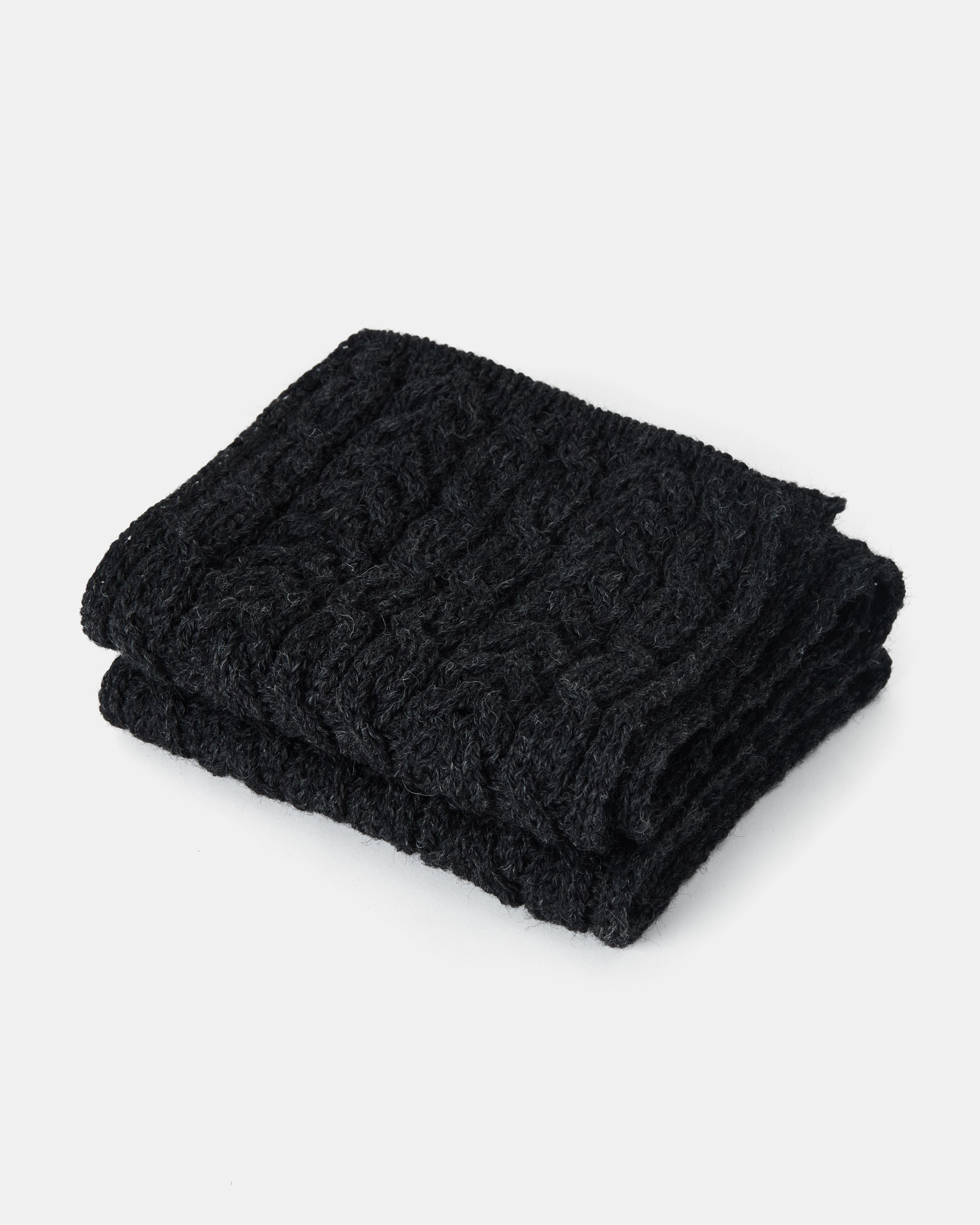 A neatly folded black knitted scarf, made from Heritage Worsted Wool, is displayed against a plain white background. The unisex-scarf features a cable knit pattern, giving it a textured and cozy appearance. This is the Aran Irish Knit Cable Scarf - B386 by Mjölkshop.se.