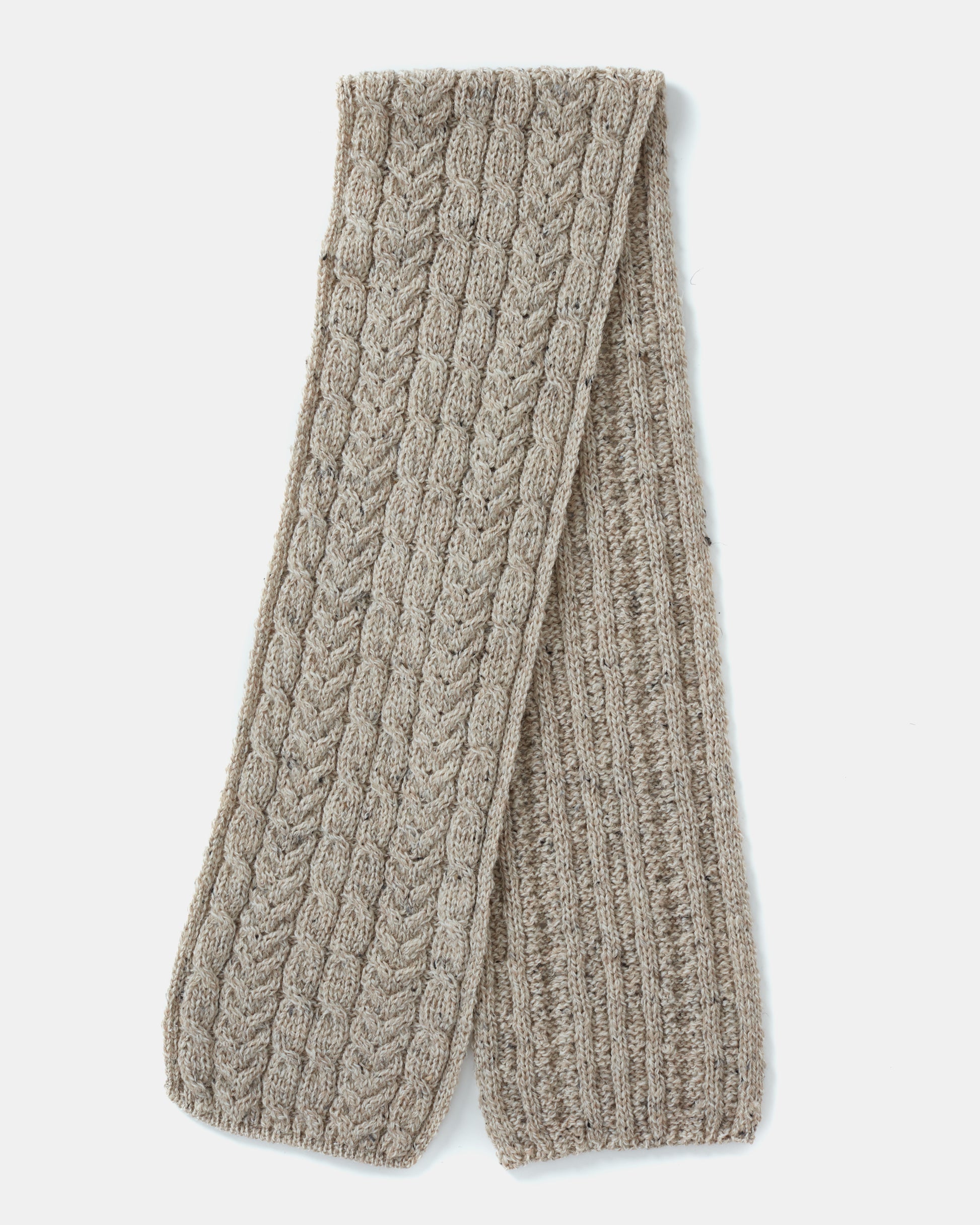 A folded beige knit unisex-scarf with a cable pattern made from Heritage Worsted Wool, the Aran Irish Knit Cabel Scarf - B386 by Mjölkshop.se. The scarf has a slightly speckled texture, adding a cozy and rustic feel to the design. It is laid flat against a white background.